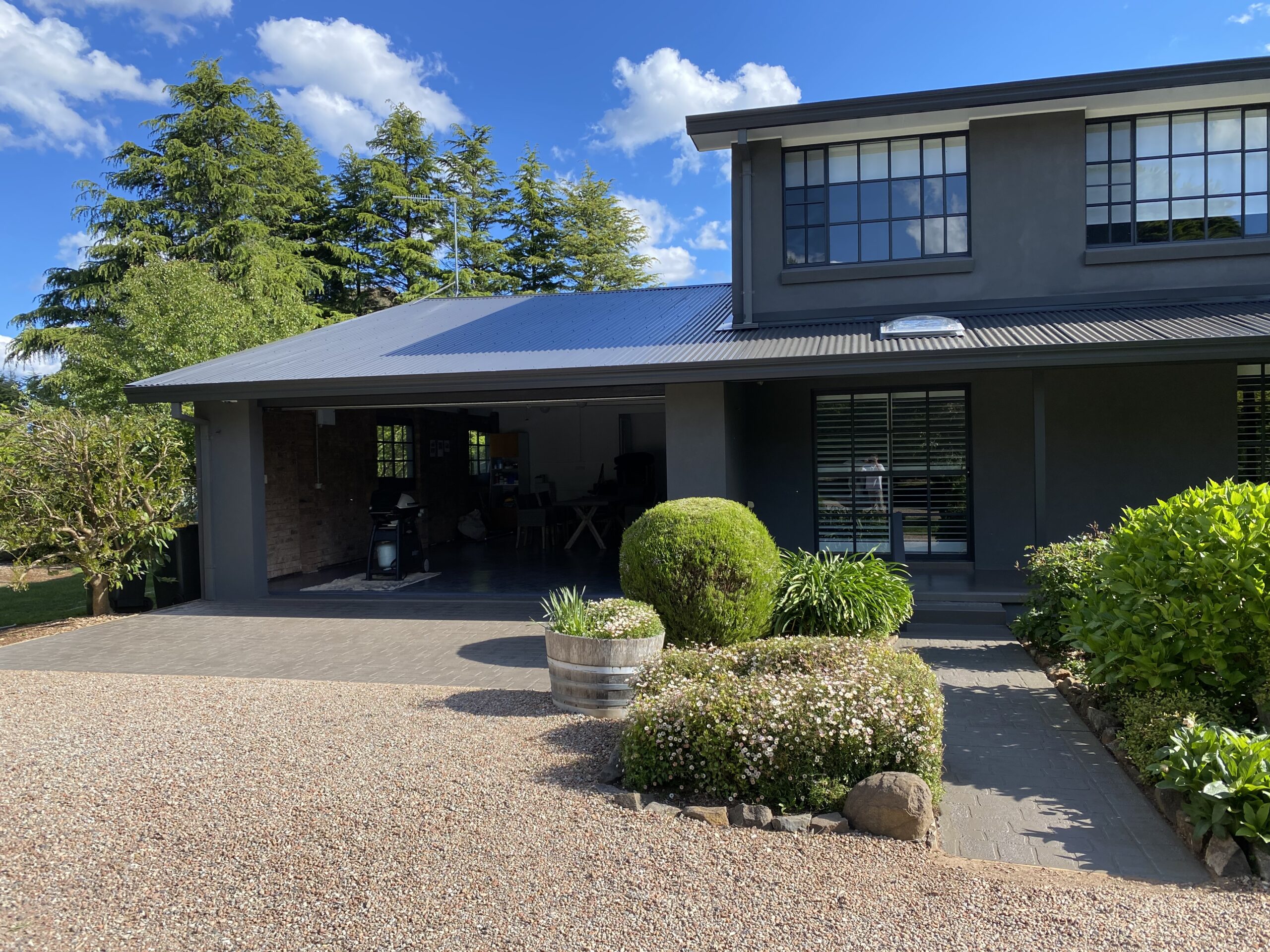 Modern exterior house painted in charcoal grey with black window frames, landscaped front garden, and gravel driveway in a Southern Highlands property.