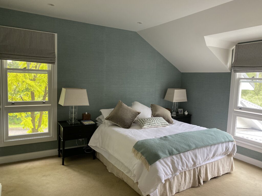Elegant bedroom with soft green feature wall, white bedding, neutral decor, and natural light from multiple windows, highlighting a serene and professionally painted interior.