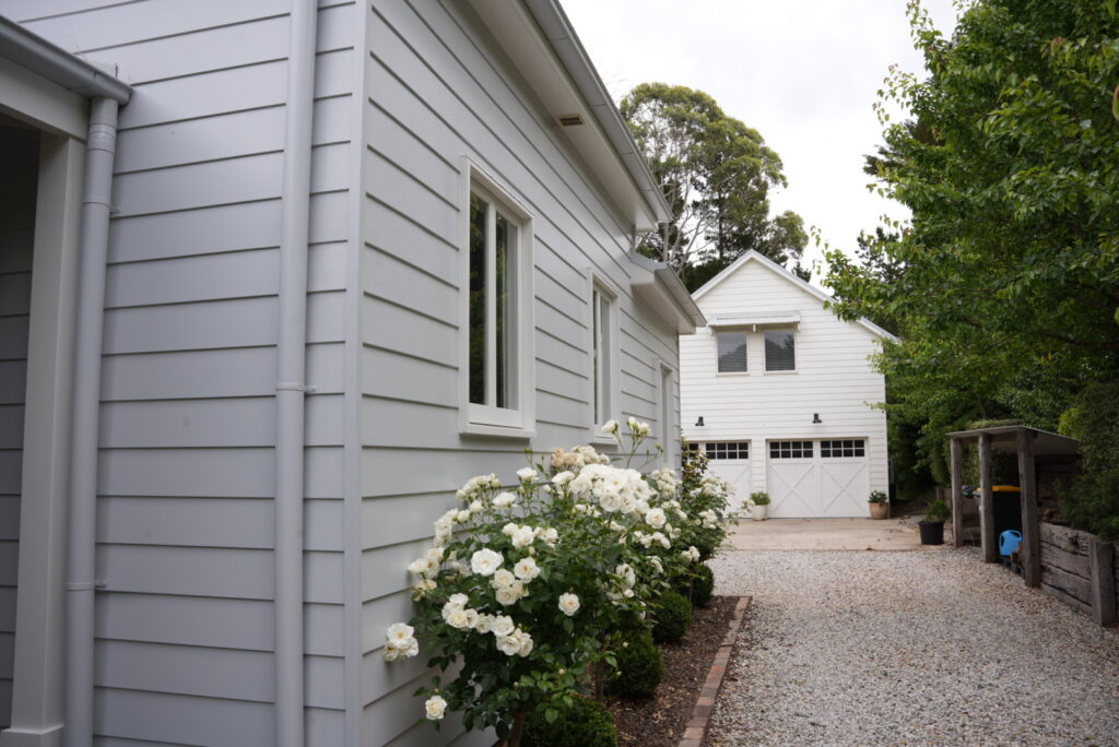 Exterior shot of white pebble driveway with white timber cladding surrounded by white roses and greenery