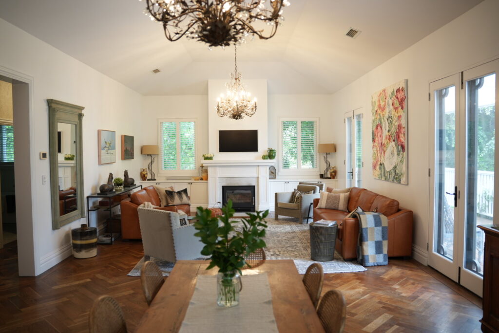 Living room featuring a fireplace is painted white with a warm light from hanging chandeliers contrasted with natural lighting from nearby windows