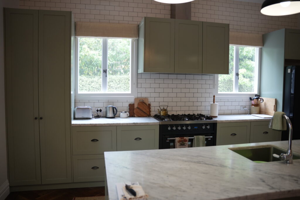 A contrast of paint colours between a light sage green cabinetry and white brick back splash with a marbel bench top