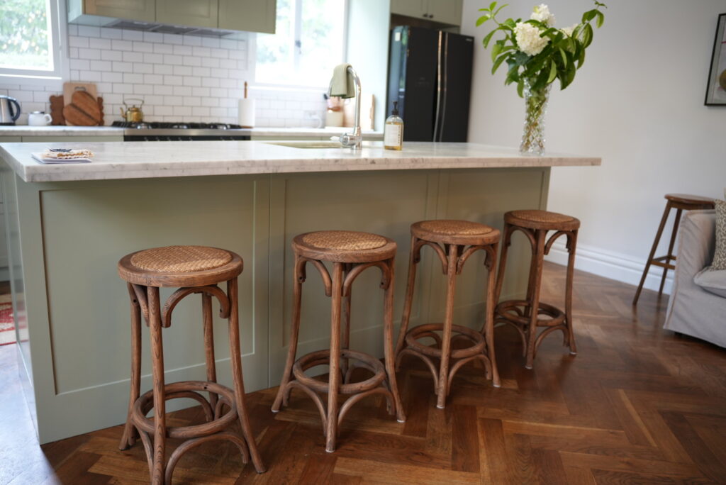 Island kitchen bench painted a pale green with a contrasting white bench top and brown wooden stools showing all three accent colours